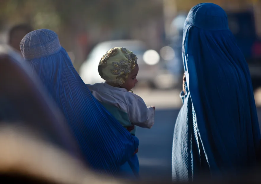 Women in blue burqas, one carrying a baby, on a street in Herat, Afghanistan