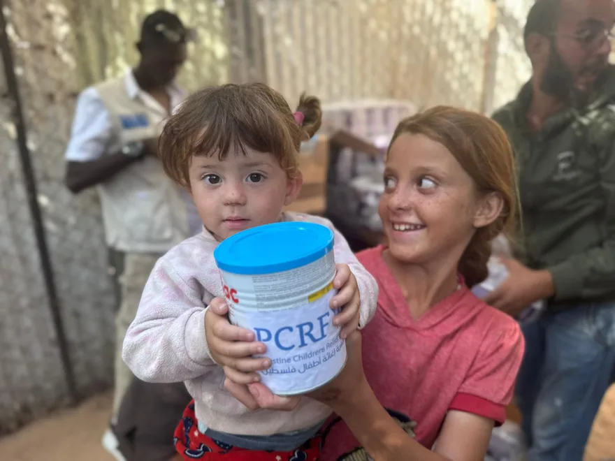 Two children at a PCRF aid distribution holding a tin of donated infant formula