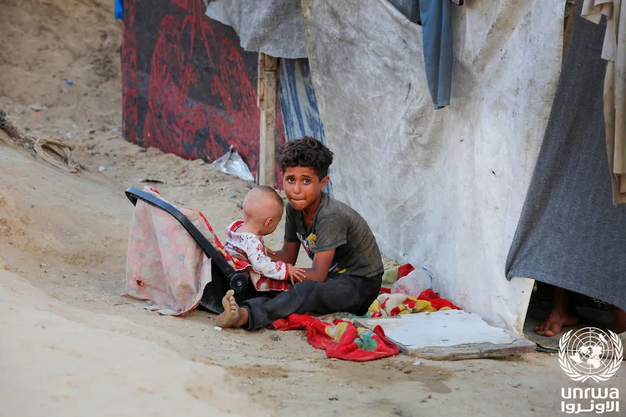 A displaced child takes care of his baby brother beside tents in Deir el-Balah, Gaza Strip